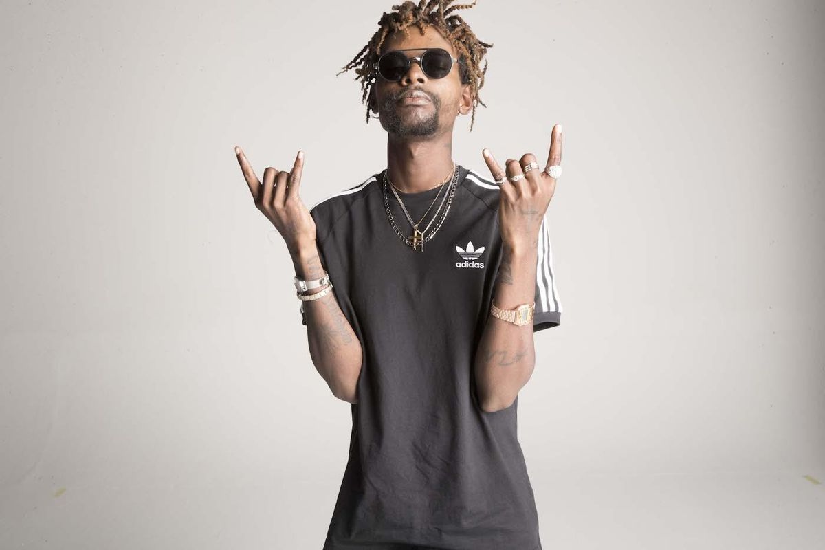 A portrait of South Africa's ATM Ranks, a black man with brown dreads, wearing black shades and an adidas t-shirt.