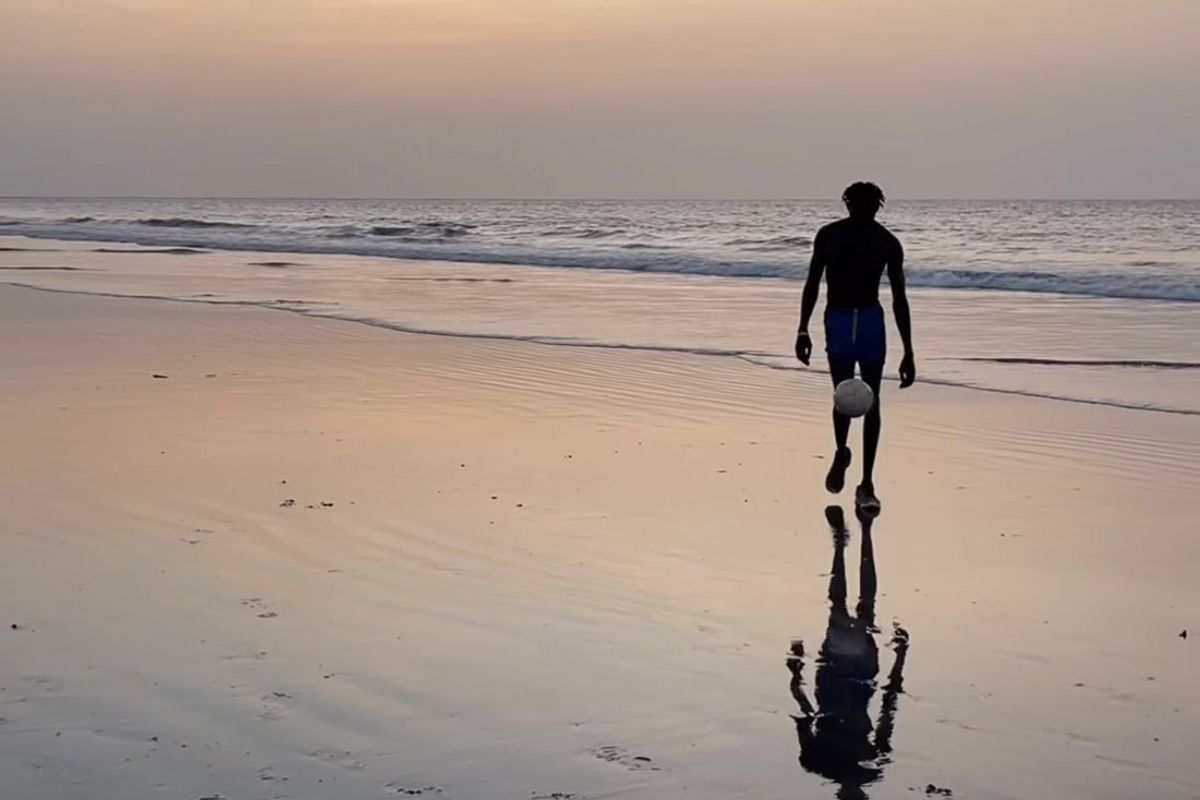 An image of a man kicking a soccer ball on a beach.