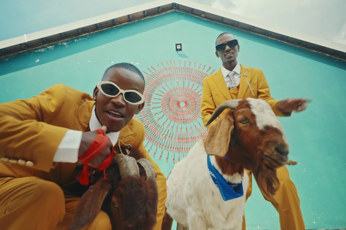 TitoM and Yuppe wearing yellow suits with silver white ties and holding on to two goats.